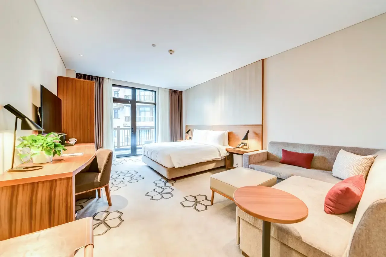 Bright hotel guest room with a bed, sofa, desk and balcony door