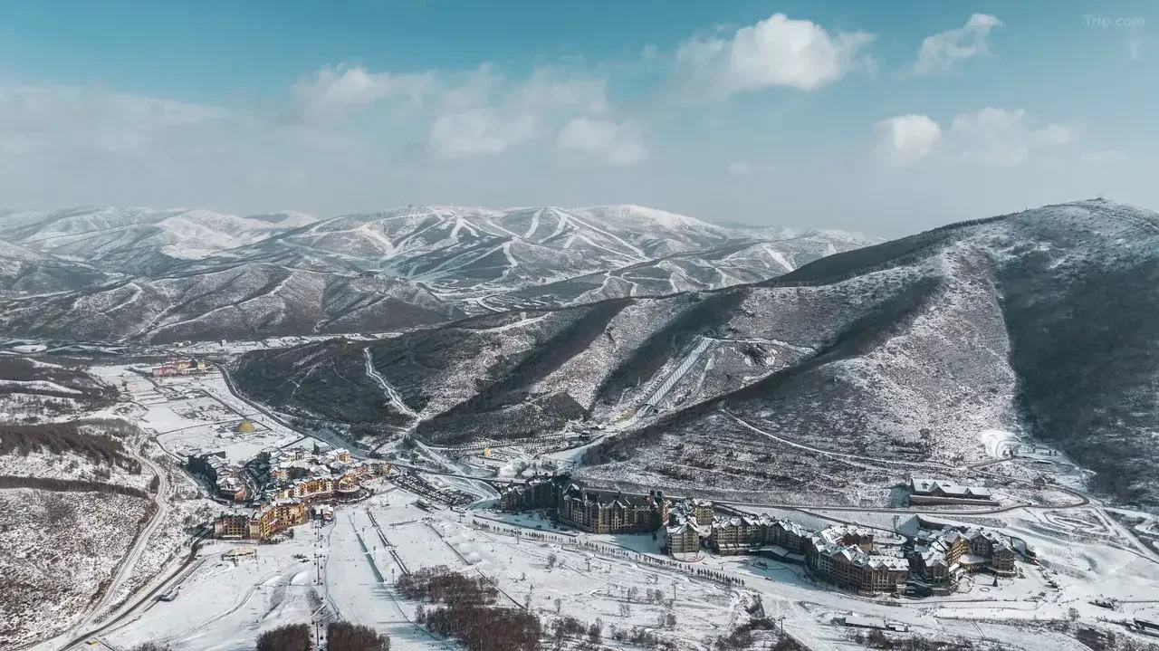 Aerial view of a snow-covered resort village, ski runs and surrounding mountain ridges