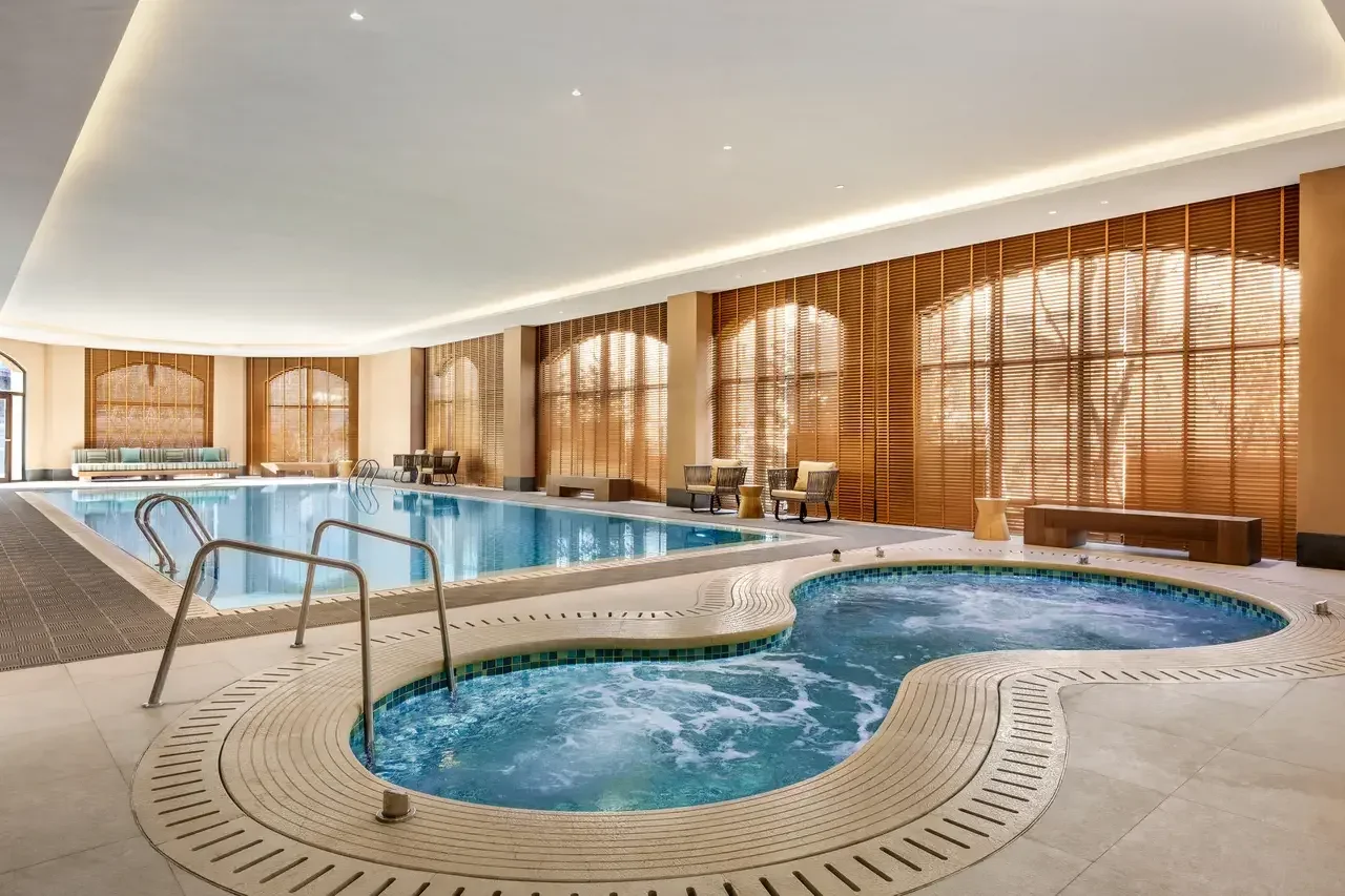 Indoor swimming pool and circular whirlpool beside tall windows