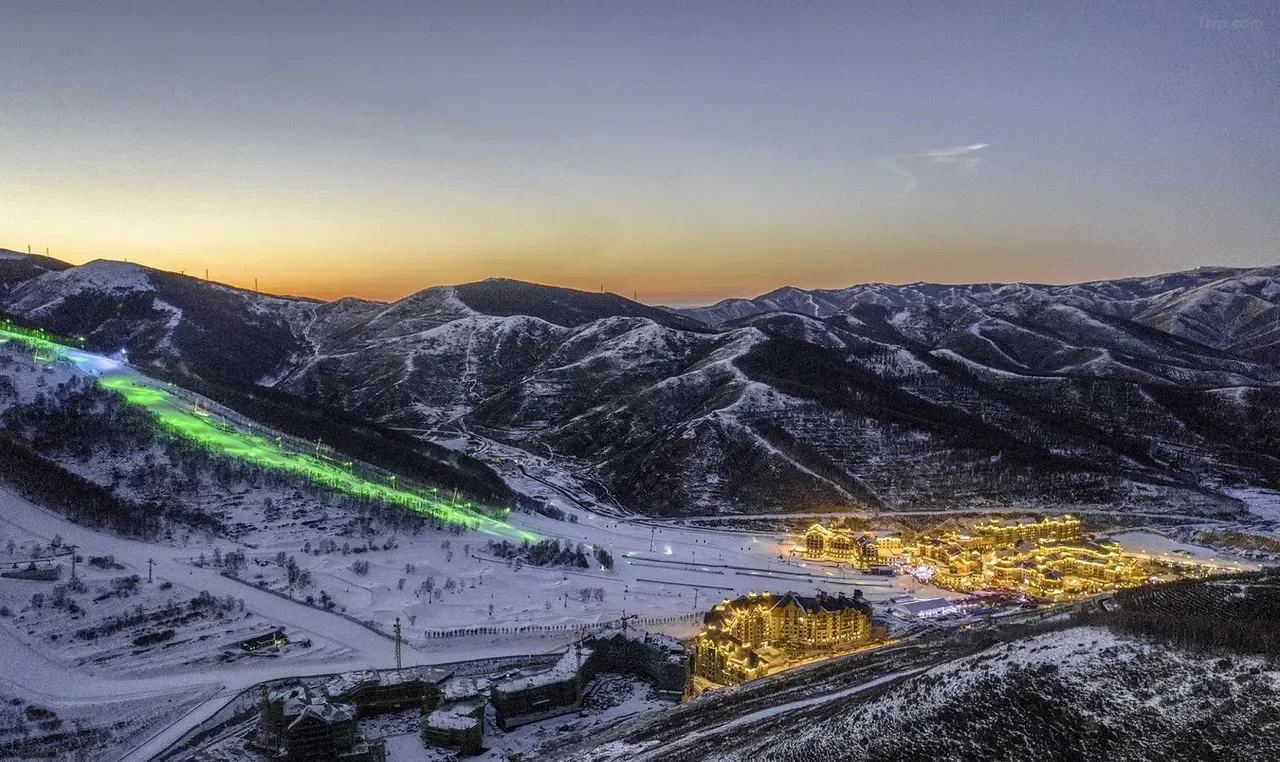 Illuminated resort buildings and ski slopes in the snowy mountains at sunset